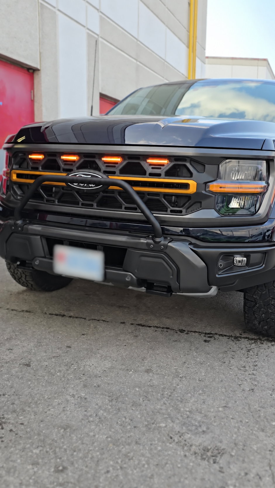 Glossy black Ford truck with reflections across the hood and its plate blurred